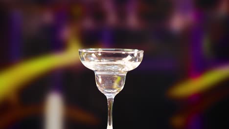 a martini glass fills with liquid against a colorful, blurred background, captured in slow motion with dramatic lighting