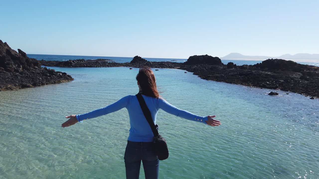 Lobos Island in the Canary Islands: Woman standing on a pier with arms outstretched, feeling free in front of a natural pool. Fuerteventura