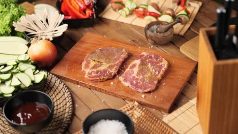 chef applying grained salt on raw piece of steak surrounded by vegetables