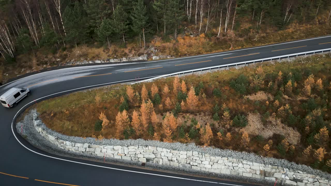 campervan conduciendo en una sinuosa carretera de montaña rodeada de árboles de otoño y bosque de hoja perenne