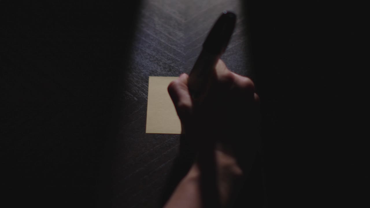 Slow motion close up footage of a hand writing out "!" on a paper note and placing it on a table. Shot in dramatic lighting for an impressive title or transition