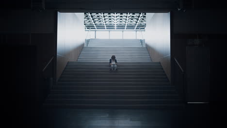 Lonely teen guy sitting on dark staircase alone. Schoolboy hiding in empty hall.
