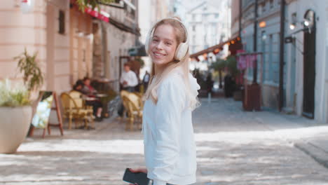 back view of happy caucasian female tourist listening to music via headphones walking on city street