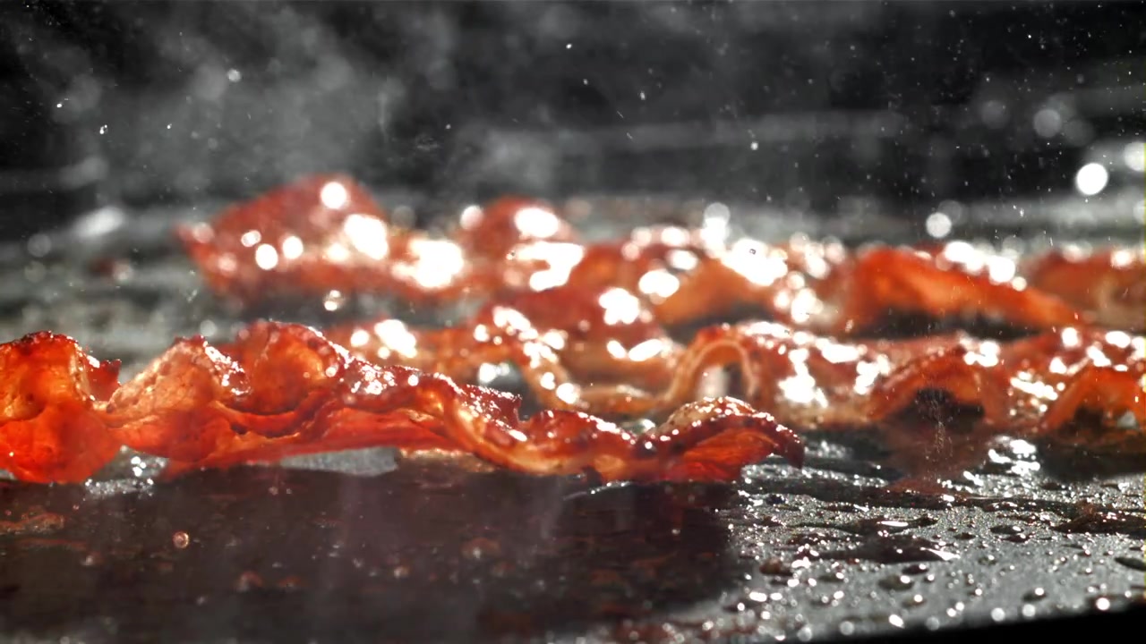Nærbillede af sprødt bacon, der syder og steger på en varm stegeplade