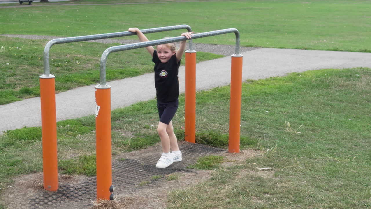 A young child shows off amazing skills by flipping upside down on monkey bars in an open park on a sunny day