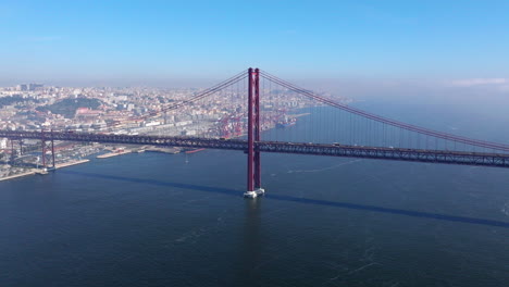 aerial drone wide establishing shot of iconic and famous lisbon red bridge by christ statue in lisbon, lisboa, portugal. sunny, bright, blue sky with clouds