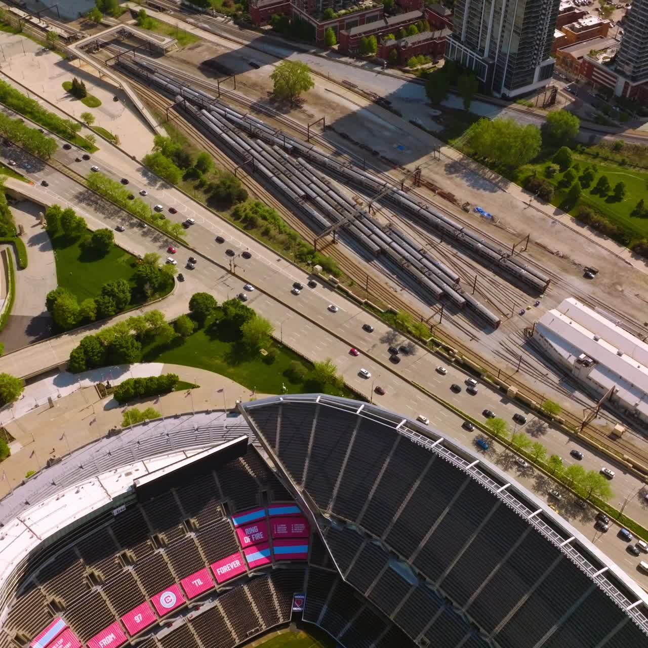 Empty Soldier Field Stadium neighboring busy highway and railway depot. Numerous green zones of the area. Sunny day backdrop. Top view