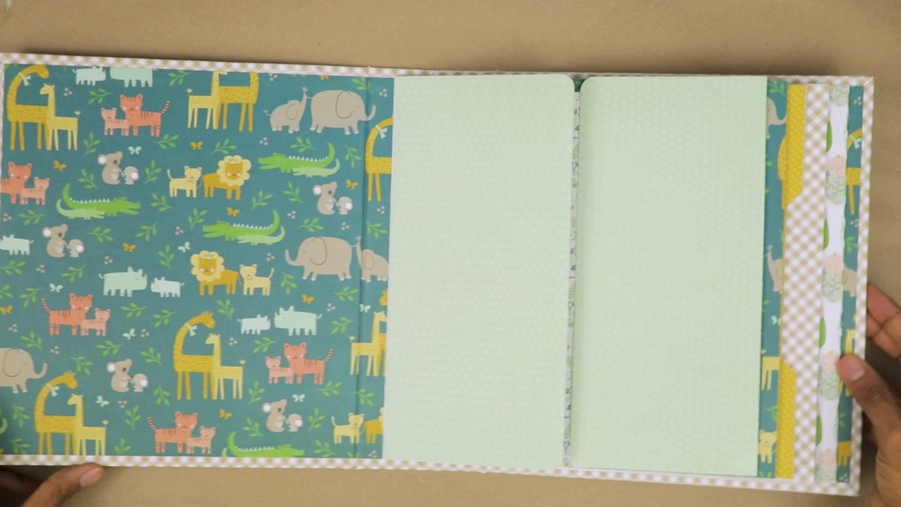 Mani che assemblano un album scrapbook colorato per bambini con pagine a tema animale, su sfondo beige