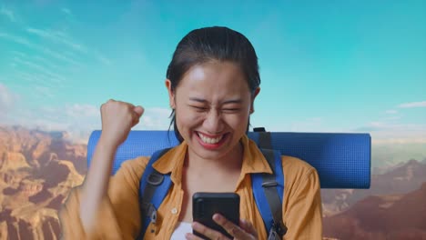 Close Up Of Asian Female Hiker With Mountaineering Backpack Looking At The Smartphone And Screaming Goal Celebrating The Success While Traveling At The Top Of Mountain