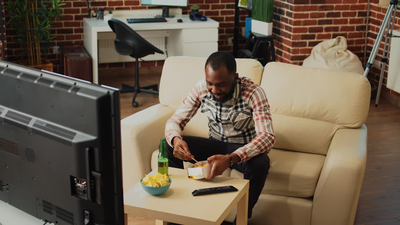 African american guy eating noodles in living room