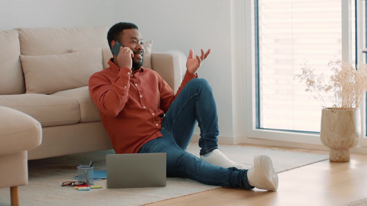 Young Man Talking on Smartphone While Sitting on Floor in Living Room