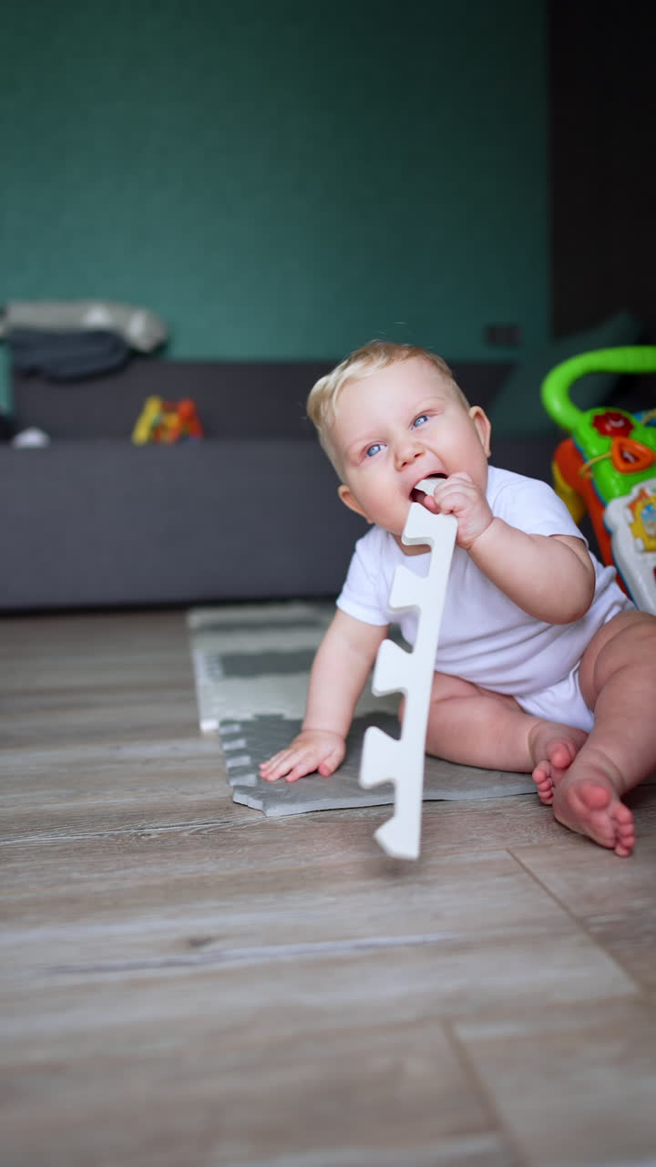 Small baby boy sits on the floor in the room. Kid chews the toys as he has teething troubles. Vertical video.