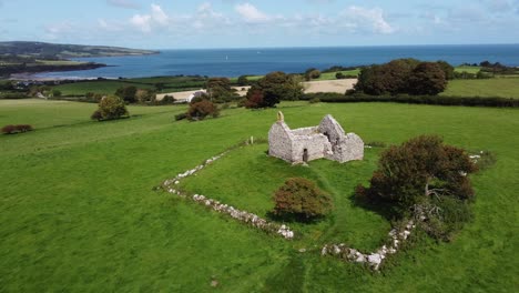 vista aérea descendiendo sobre capel iligwy capilla en ruinas en la costa de la isla de anglesey, gales del norte