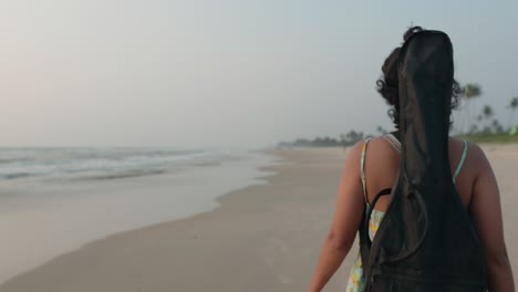 a young indian musician, with her guitar case on her back, immerses herself in the serene beauty of the beach, creating a harmonious fusion of music and nature