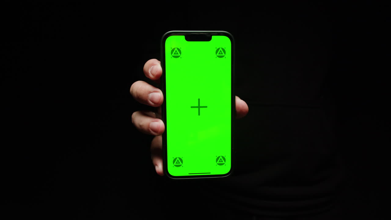 Smartphone with chroma key screen on black background close-up. Green screen on mobile phone in hand.