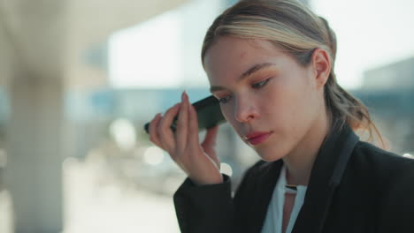 close up of female lawyer attentively listening to voice note from client while standing outside modern glass building reflecting surroundings