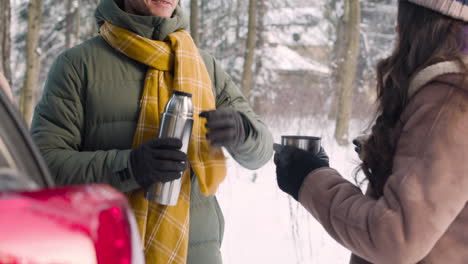 man offers a hot drink from a thermos to her wife while they talking