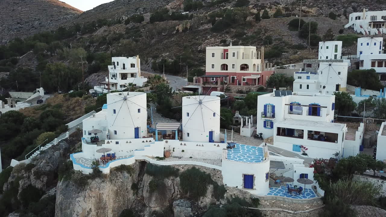 Greece,Leros Island, Panteli Village, Drone footage of the 2 white windmills on a big rock renovated as a hotel or residence,camera turns around the buildings slightly during sunset.