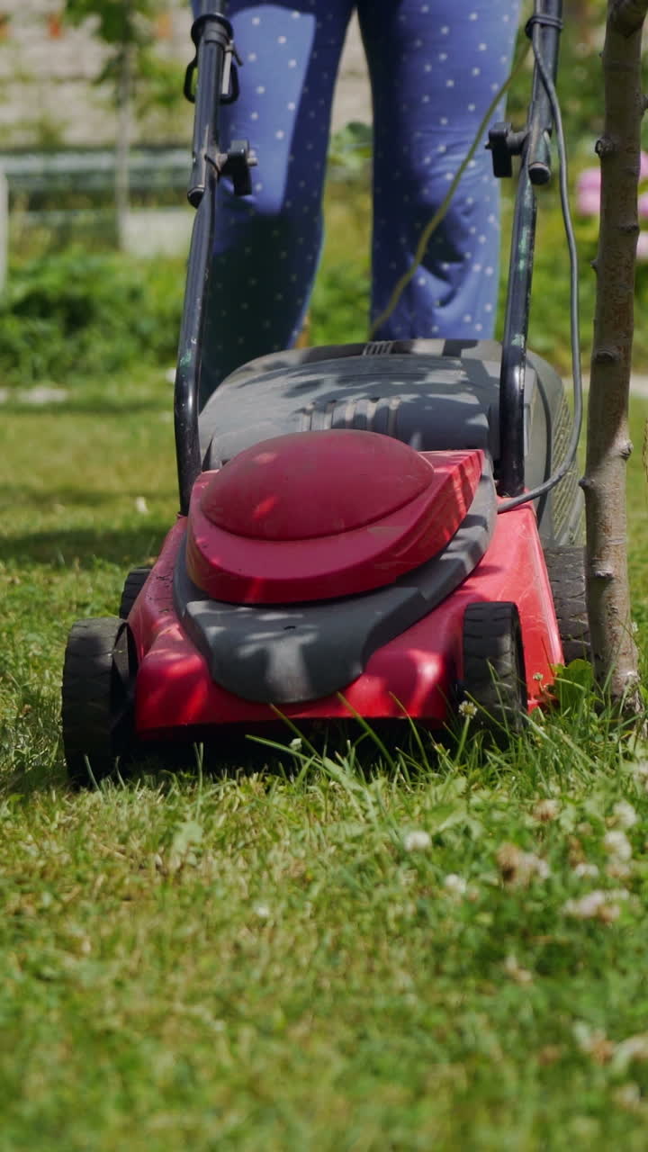 Farmer woman mowing lawn in residential back garden.. Vertical video