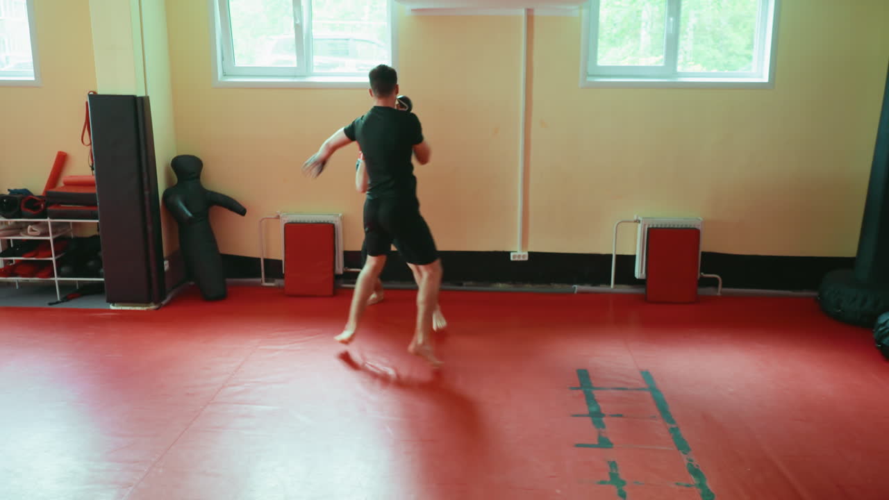 Two wrestlers practicing sparring in gym on red mat, engaged in close combat stance, wearing gloves, barefoot, training martial arts, focusing on power, endurance, agility, discipline, fighting technique
