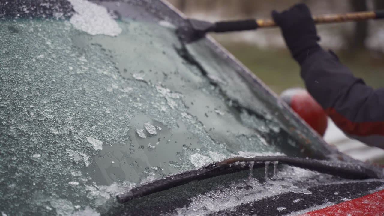 Man cleaning and scraping ice from car windshield in snow slowmo
