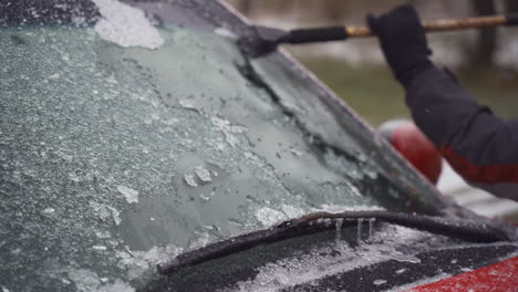 man cleaning and scraping ice from car windshield in snow slowmo