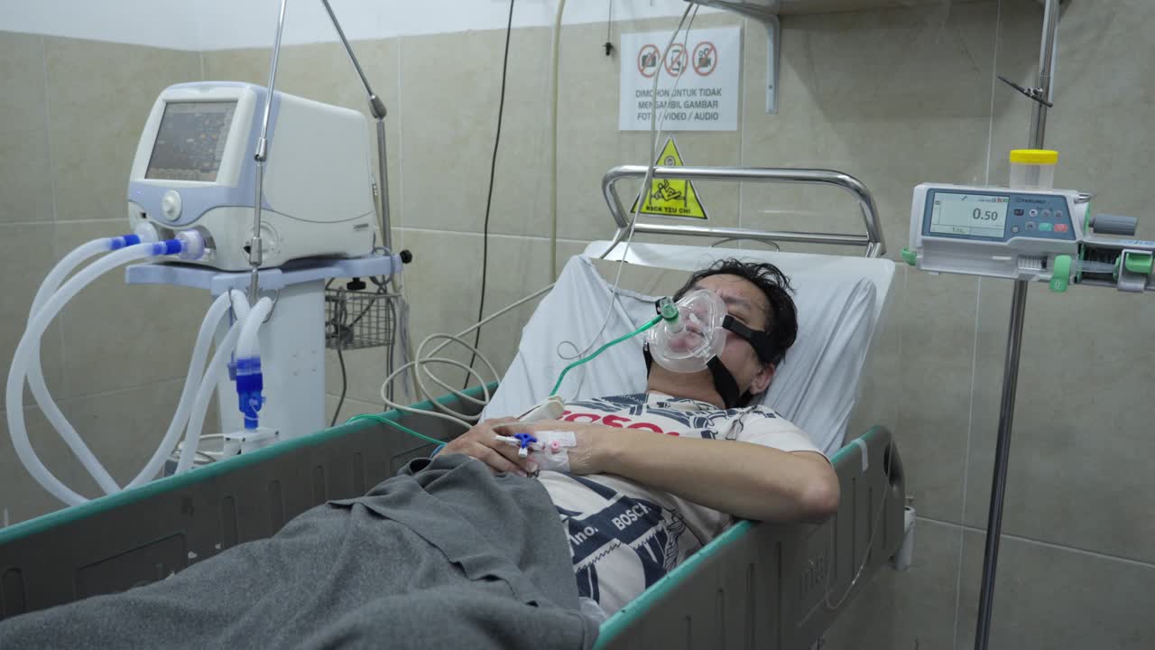 Paciente en cama de hospital con mascarilla de oxígeno, tosiendo mientras duerme, rodeado de monitores médicos y equipo respiratorio. Plano general.