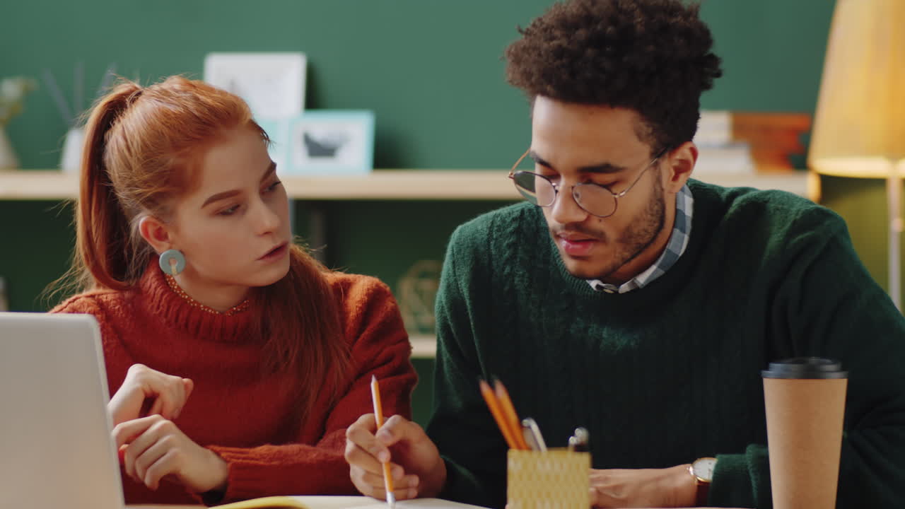dos adultos jóvenes que colaboran en un proyecto o discuten algo en un entorno de trabajo casual.