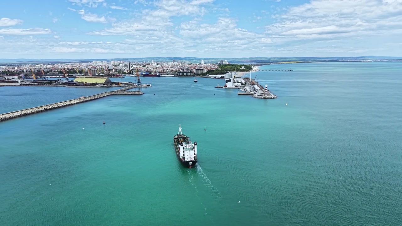 Udsigt over en havn med skibe og byens skyline i et kystområde under en klar himmel i dagtimerne.
