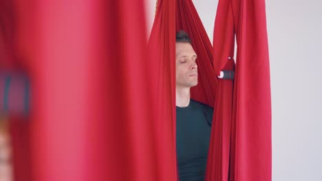 concentrated-man-sits-in-fly-yoga-hammock-with-closed-eyes