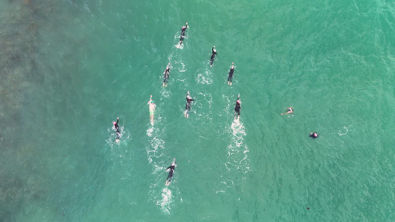 Aerial footage of swimmers practicing in clear turquoise ocean waters near Port Campbell, Australia, showcasing teamwork and athleticism