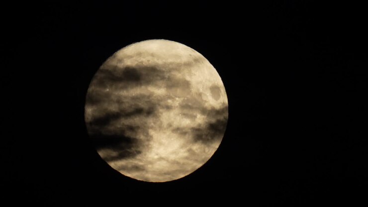 A lua cheia atravessa o céu noturno por trás de nuvens escuras e sinistras