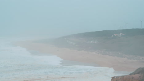 Neblige-Meeresküste-Mit-Fernen-Windkraftanlagen-In-Nazare,-Portugal