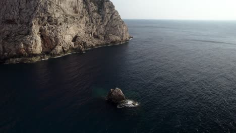 aerial shot of the small rock and huge cliffs and a dark calm mediterranean sea surface