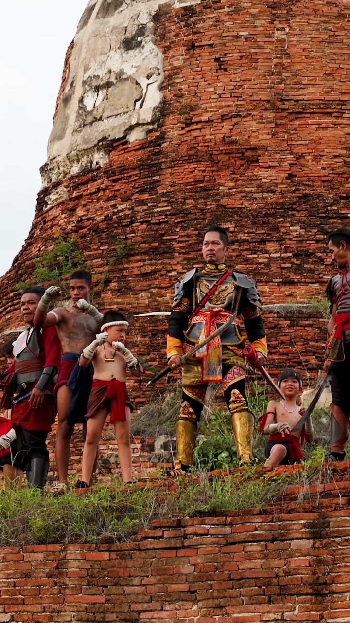 Historical reenactors in traditional armor pose with weapons before an ancient red brick temple.