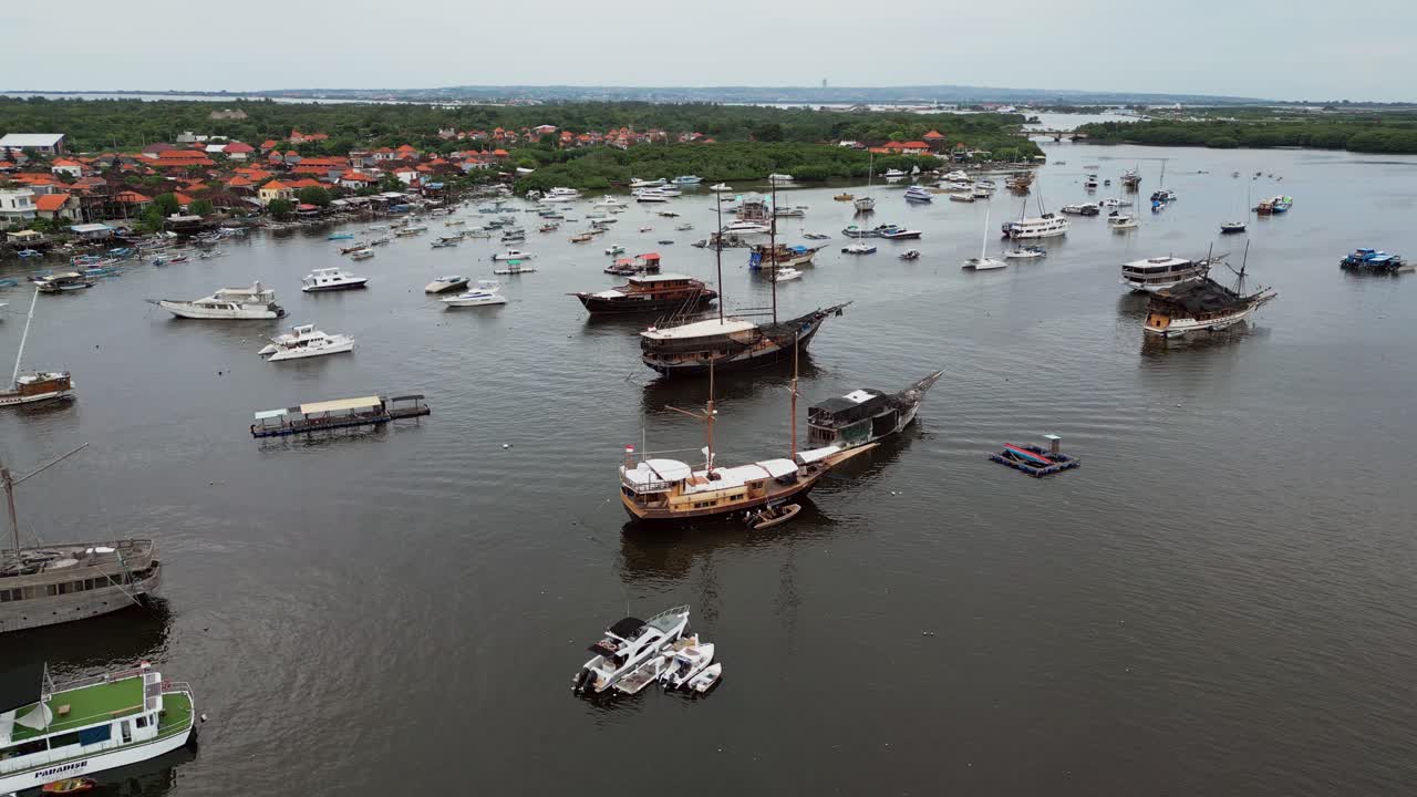 Højt engel dronebillede, der fanger klassiske træbåde for anker i en rolig havn på Bali, med glat vand, der afspejler tropisk maritimt landskab og traditionel søfartsstemning