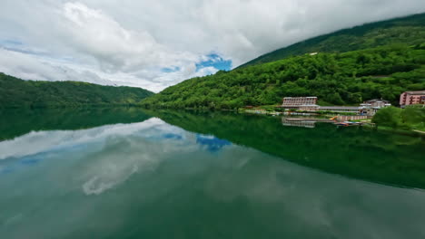 Lago-di-levico-with-lush-green-hills-and-calm-waters-on-a-cloudy-day,-aerial-view