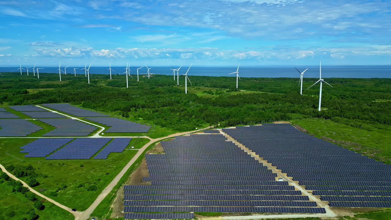 Solar panels and wind turbines on a seacoast provide renewable, efficient power - pullback aerial