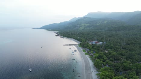 dili coastline with lush greenery, beach, and distant mountains at sunrise, aerial view