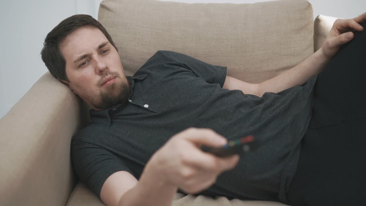 man is lying in front of the TV with remotes he is watching films in his day off