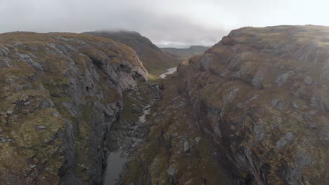 River-flowing-in-canyon-with-dark-clouds-above,-Norway-highlands,-rising-aerial