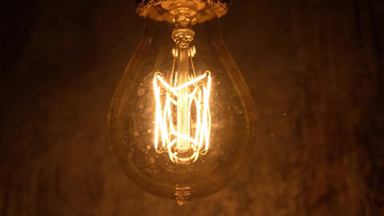 Affascinante Bagliore Caldo di una Lampadina Vintage che Illumina uno Sfondo Tenue, Mostrando l'Intricato Design del Filamento in Due Cornici Suggestive