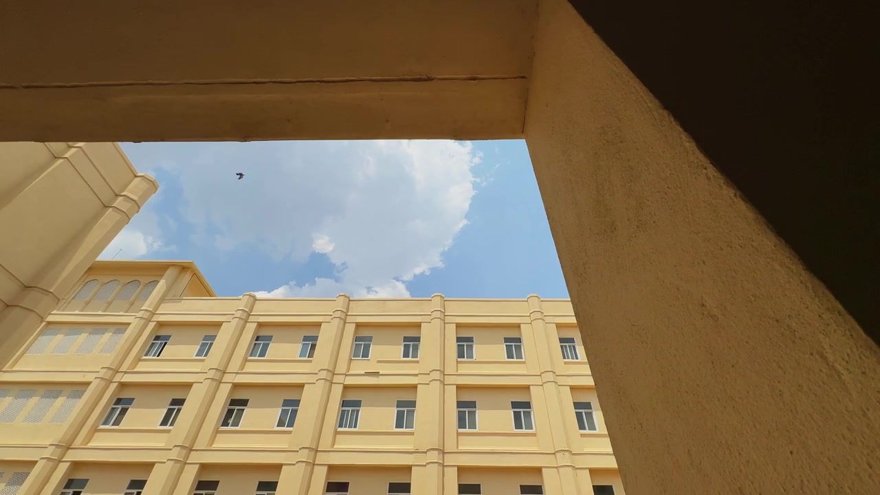 Tomada grande angular com aproximação revelando um edifício institucional de vários andares recém-construído, emoldurado pela arquitetura circundante, com janelas simétricas, fachada limpa e céu aberto