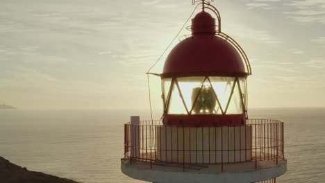 Close-up-drone-shot-of-a-lighthouse-with-sun-and-ocean-in-the-background-at-golden-hour