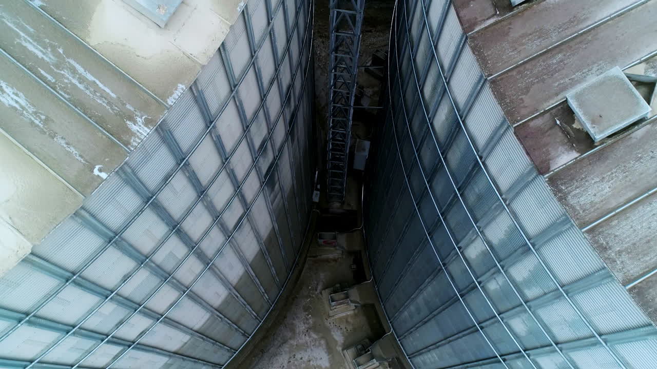 Going down among two huge metal granary tanks. Exterior footage of the modern silo complex on winter day.