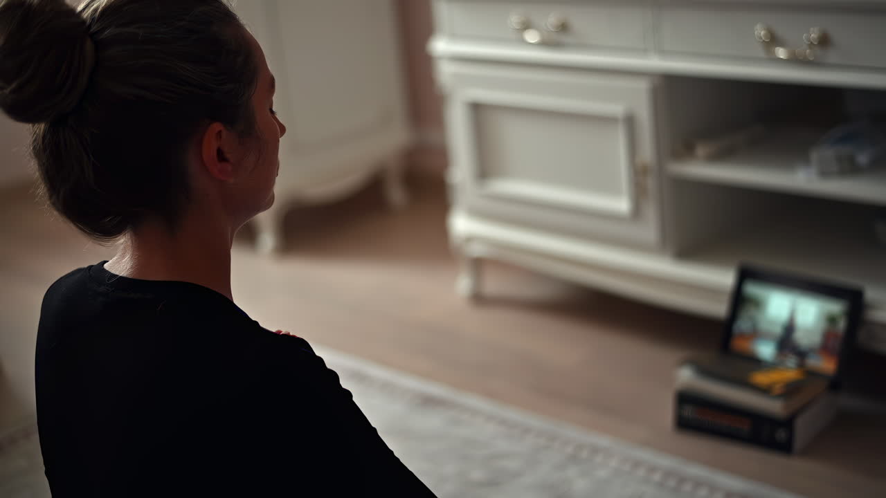 A woman practices meditation in her serene living room. She sits calmly, focusing on a screen that guides her. Soft morning light fills the area