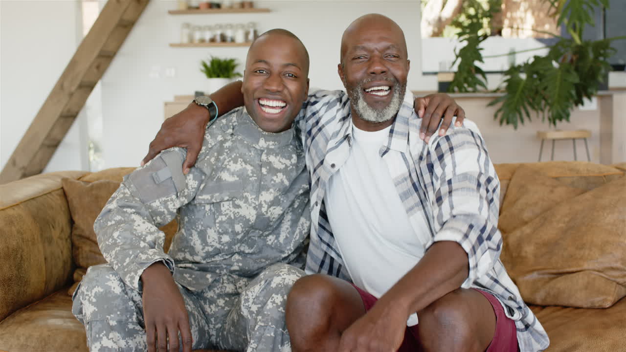 Smiling military father sitting on couch, hugging older father in casual clothes