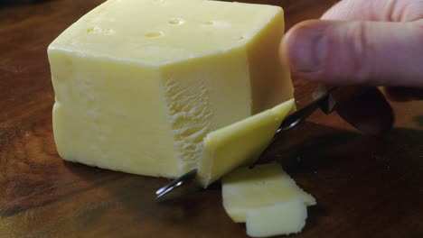 right hand with small knife cuts slices off block of swiss cheese