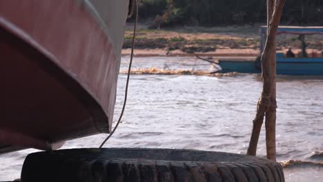 Mittlere-Aufnahme-Des-Sees-Von-Hinten-Eine-Sehr-Nahe-Bootsecke-Auf-Einem-Reifen-Mit-Einem-Blauen-Boot,-Das-Auf-Dem-Wasser-Vorbeifährt