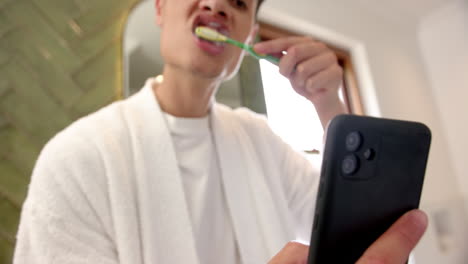 biracial man brushing teeth and using smartphone in bathroom in the morning, slow motion